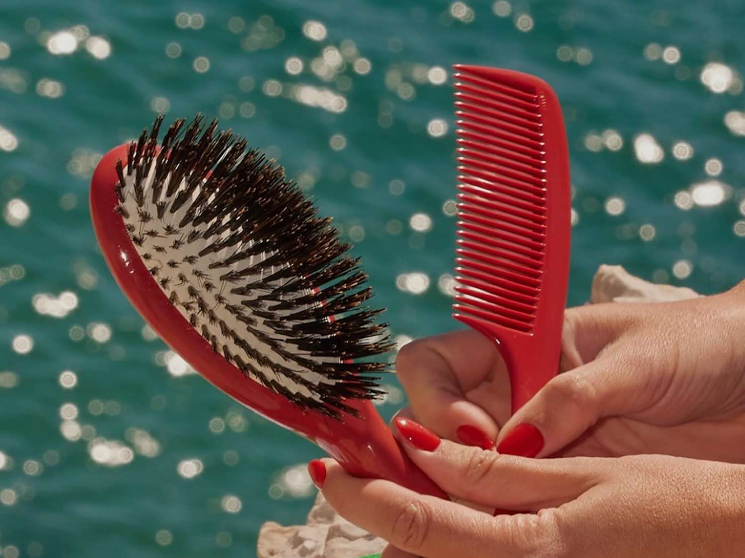 a hand holding a red brush and a red comb