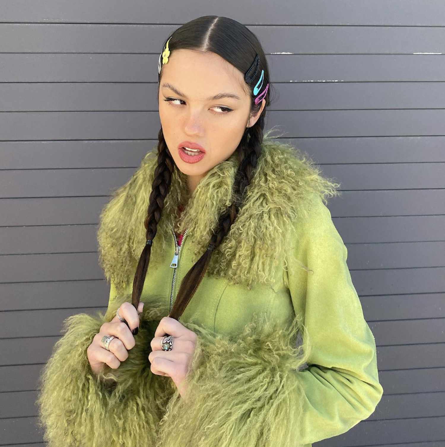 Olivia Rodrigo wears braided pigtails with multicolored hair clips and a green fluffy coat