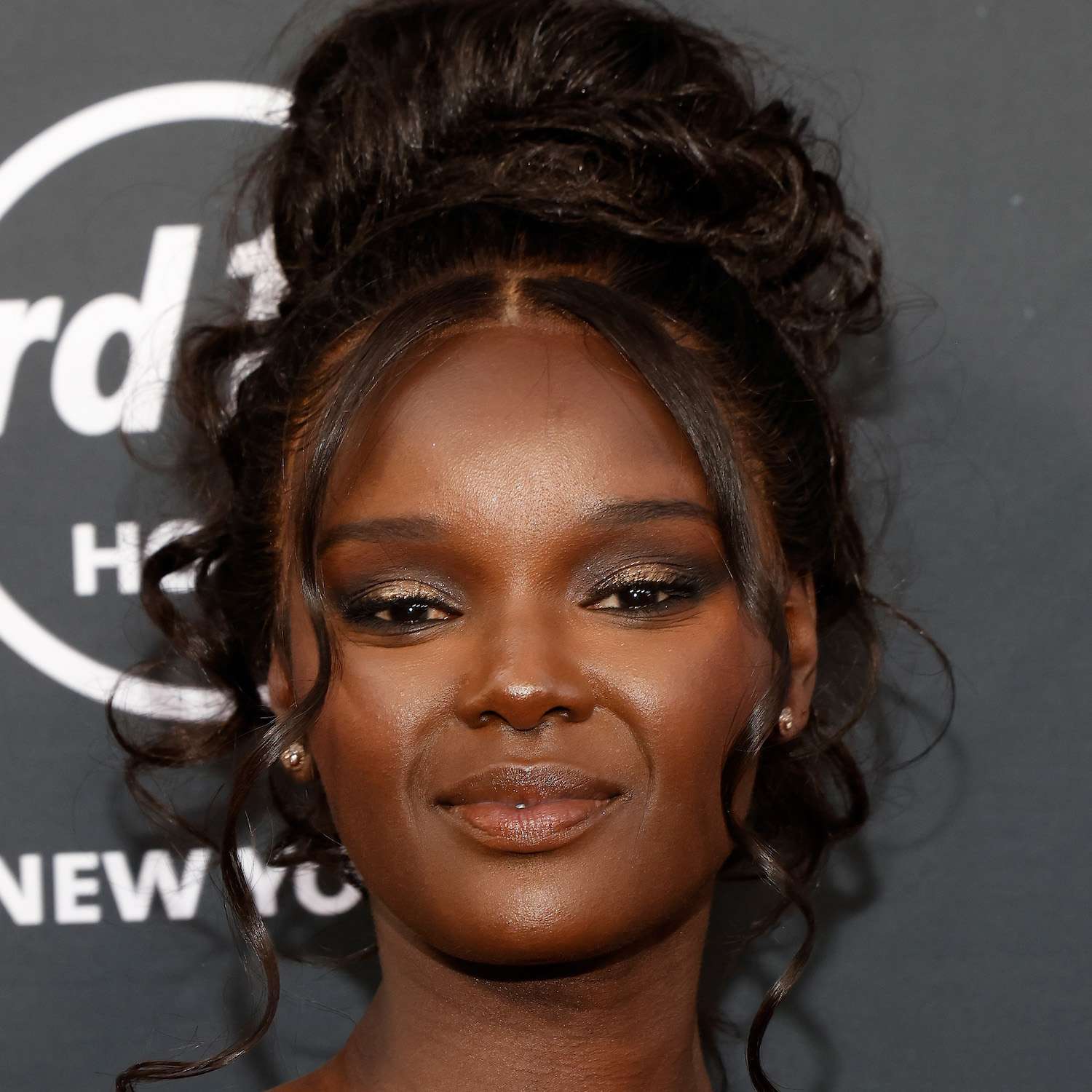 Duckie Thot wears a curly high bun updo hairstyle with face-framing tendrils