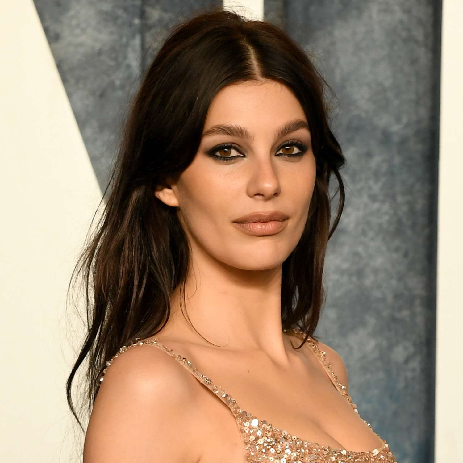 Camila Morrone wears a wavy hairstyle with a center part and face-framing layers