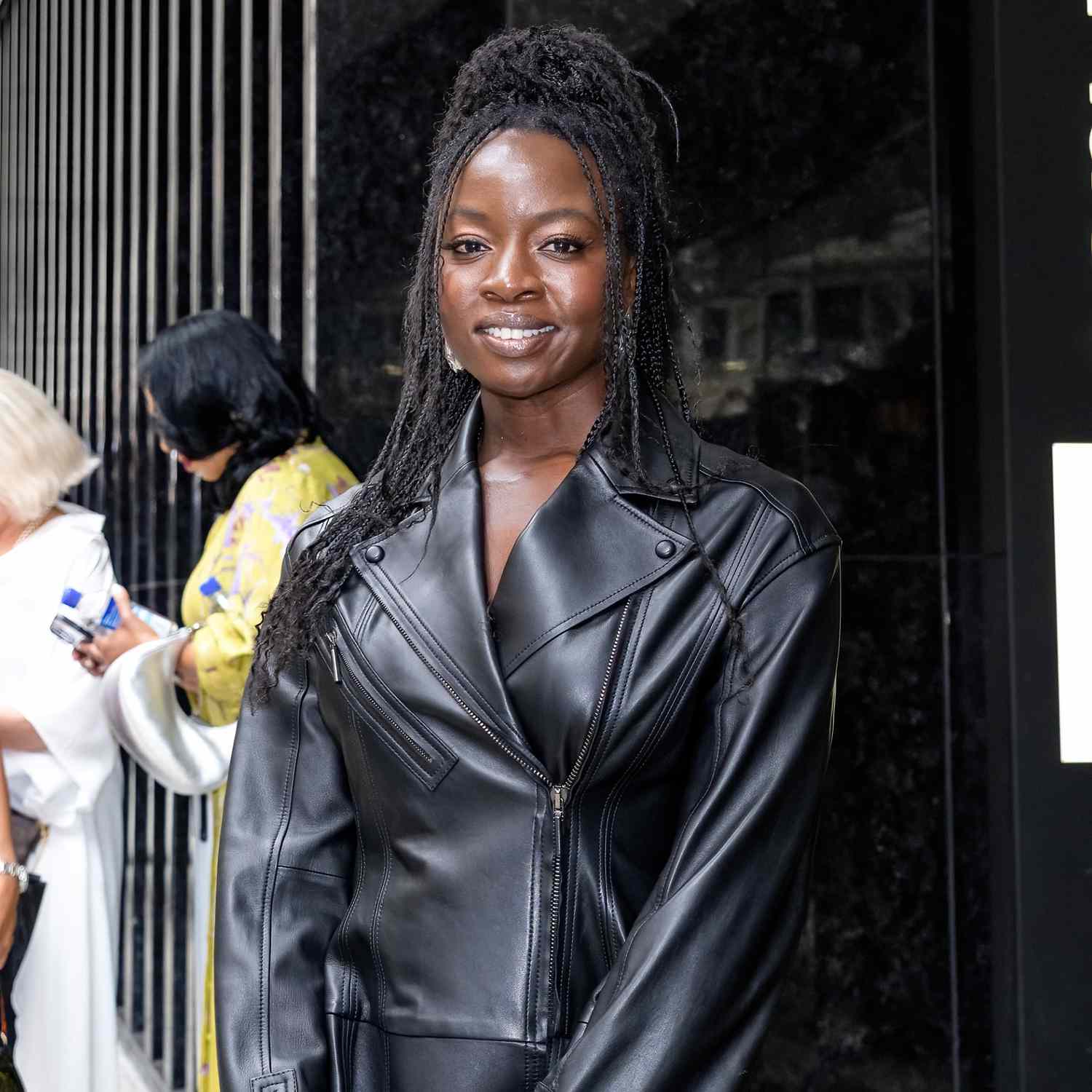 Danai Gurira smiling at camera with braided hair, a few pieces left out in the front in face-framing fashion, top section of hair pulled back into messy bun on top of head