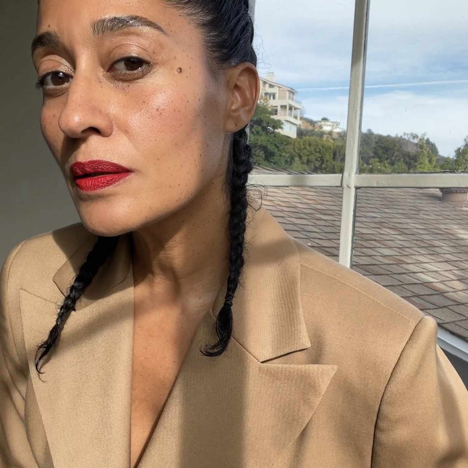 Tracee Ellis Ross wears French braided pigtails, a beige blazer, and red lipstick