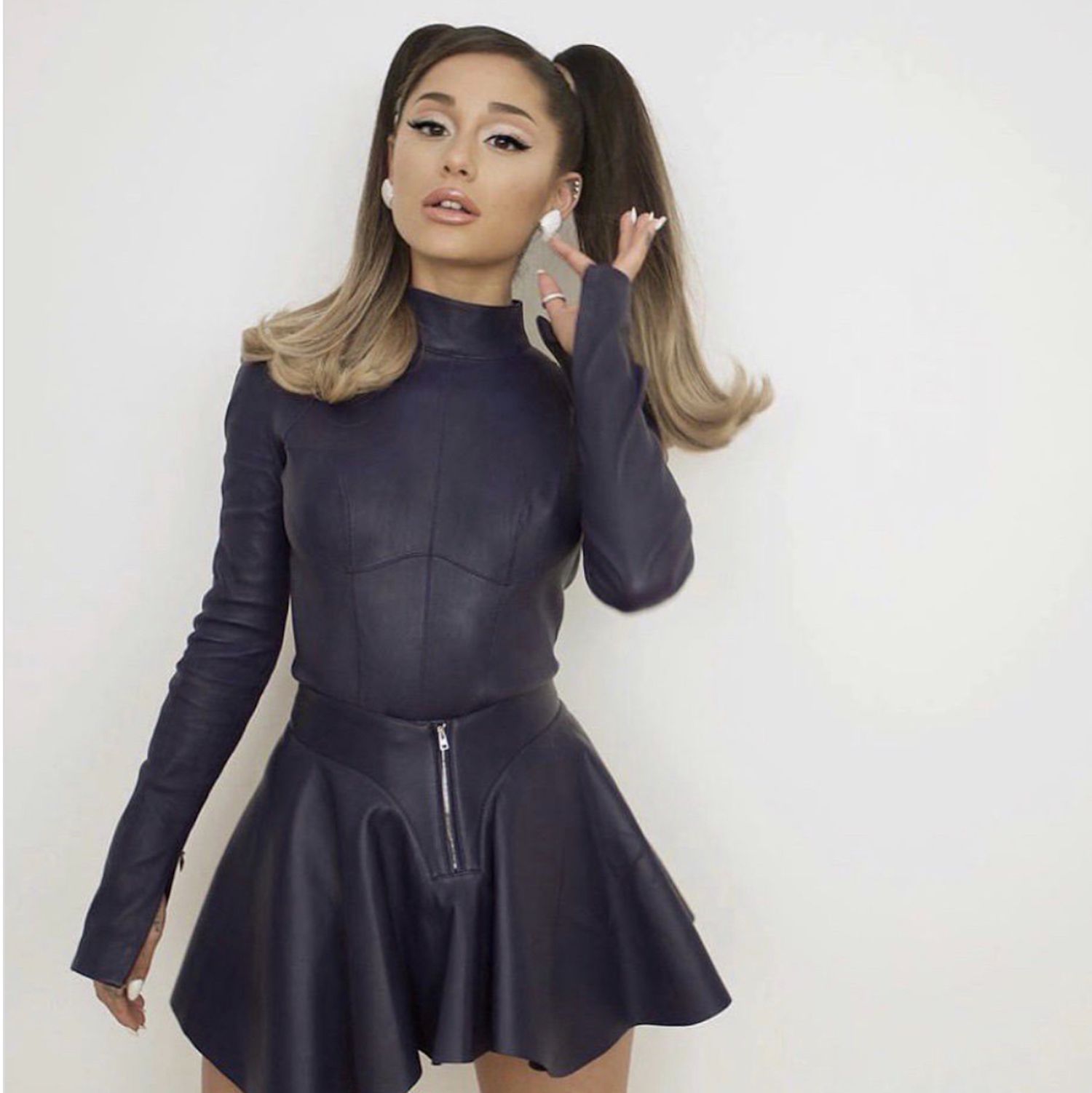Ariana Grande wears a high-neck bodysuit, leather skater skirt, and high pigtails with flipped ends