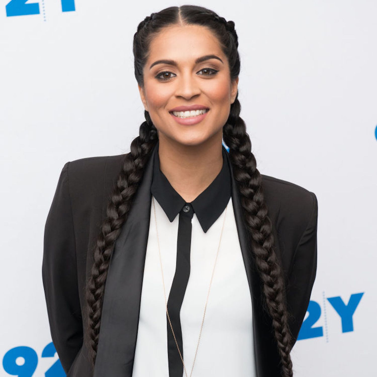 Lilly Singh wears French braided pigtails, a collared black and white shirt, and a black blazer