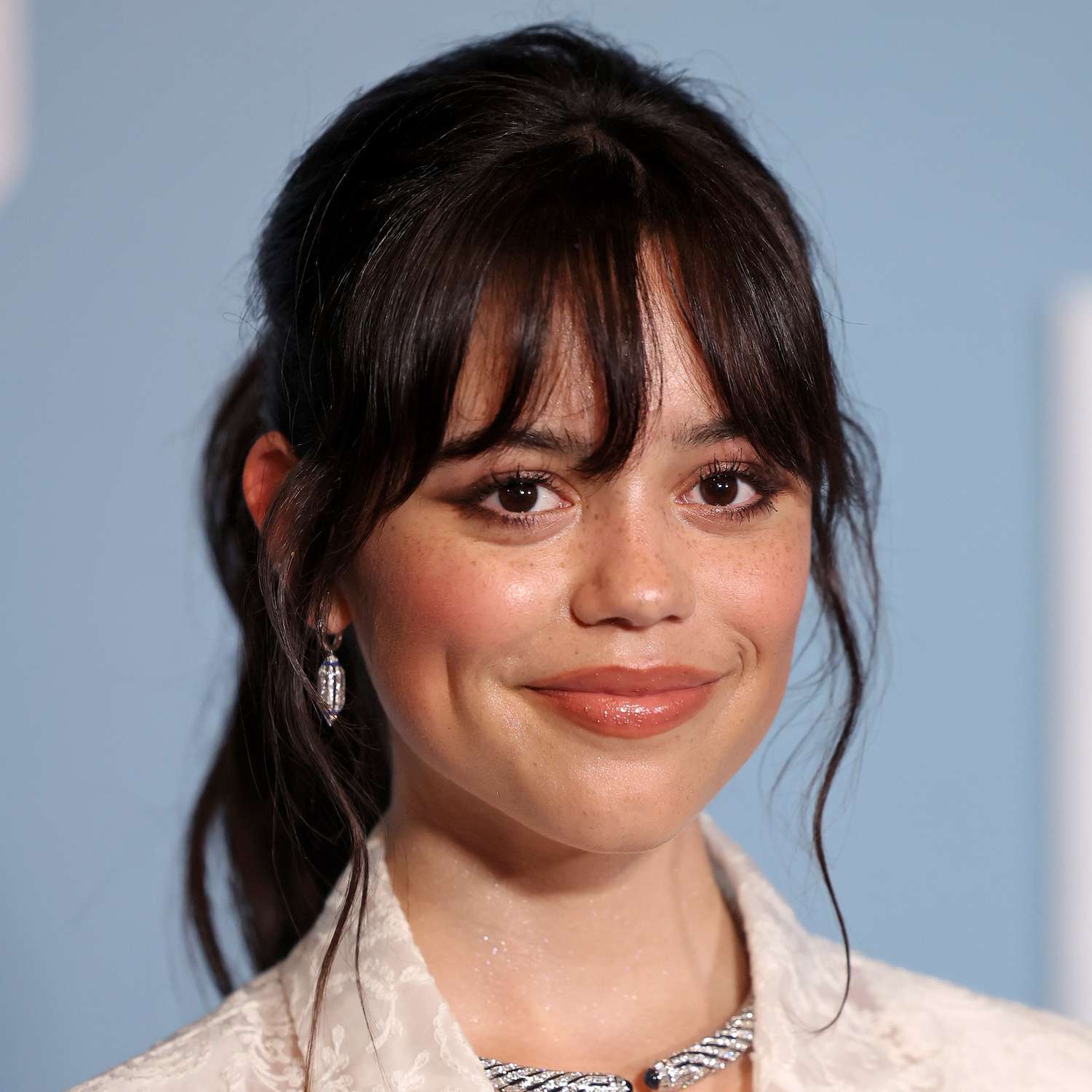 Jenna Ortega wears french bangs styled to frame her face with a mid-height ponytail at an LA premiere