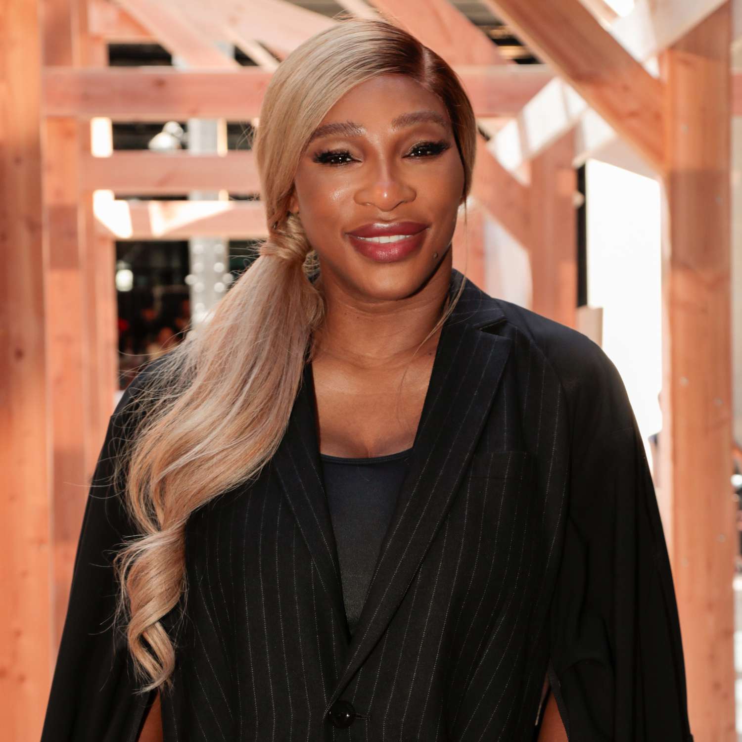 Serena Williams wears low, side swept blond in a ponytail over the shoulder of her black blazer