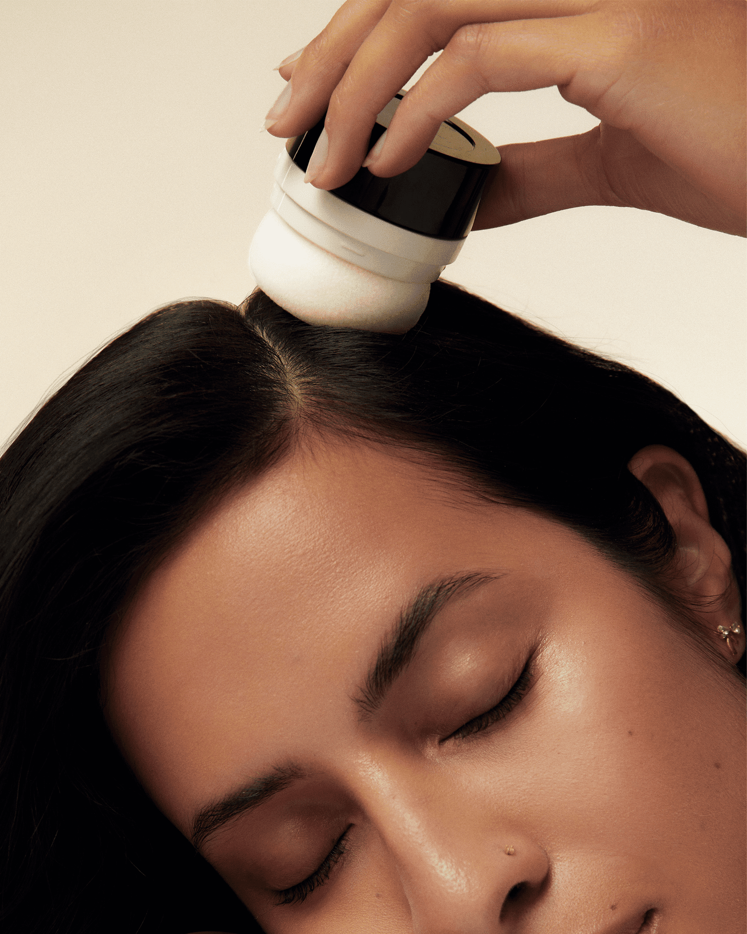 Model with long black hair applying dry shampoo pouf to her roots