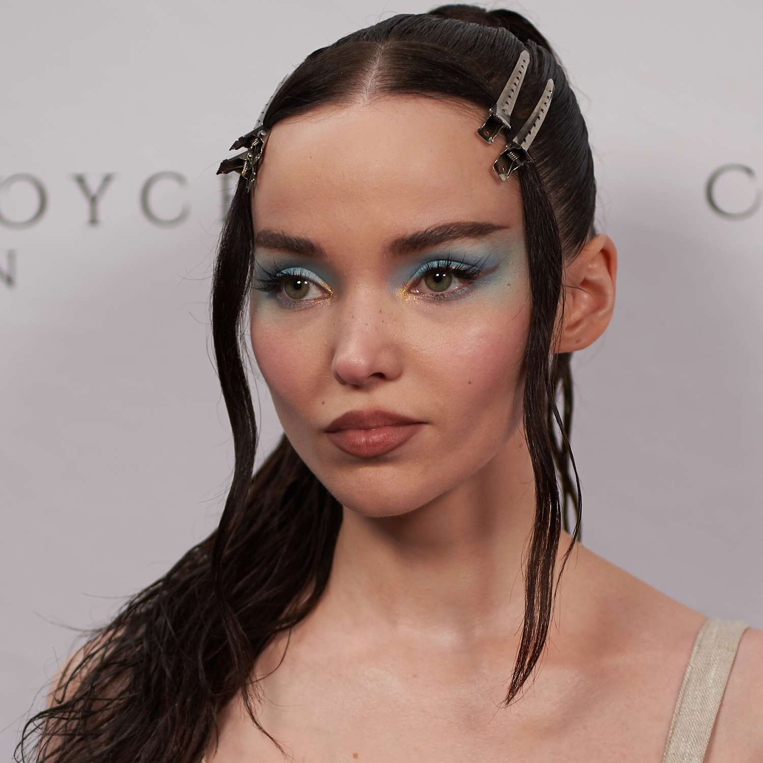 Dove Cameron wears a high ponytail and duck bill clips to hold her front pieces back off the face