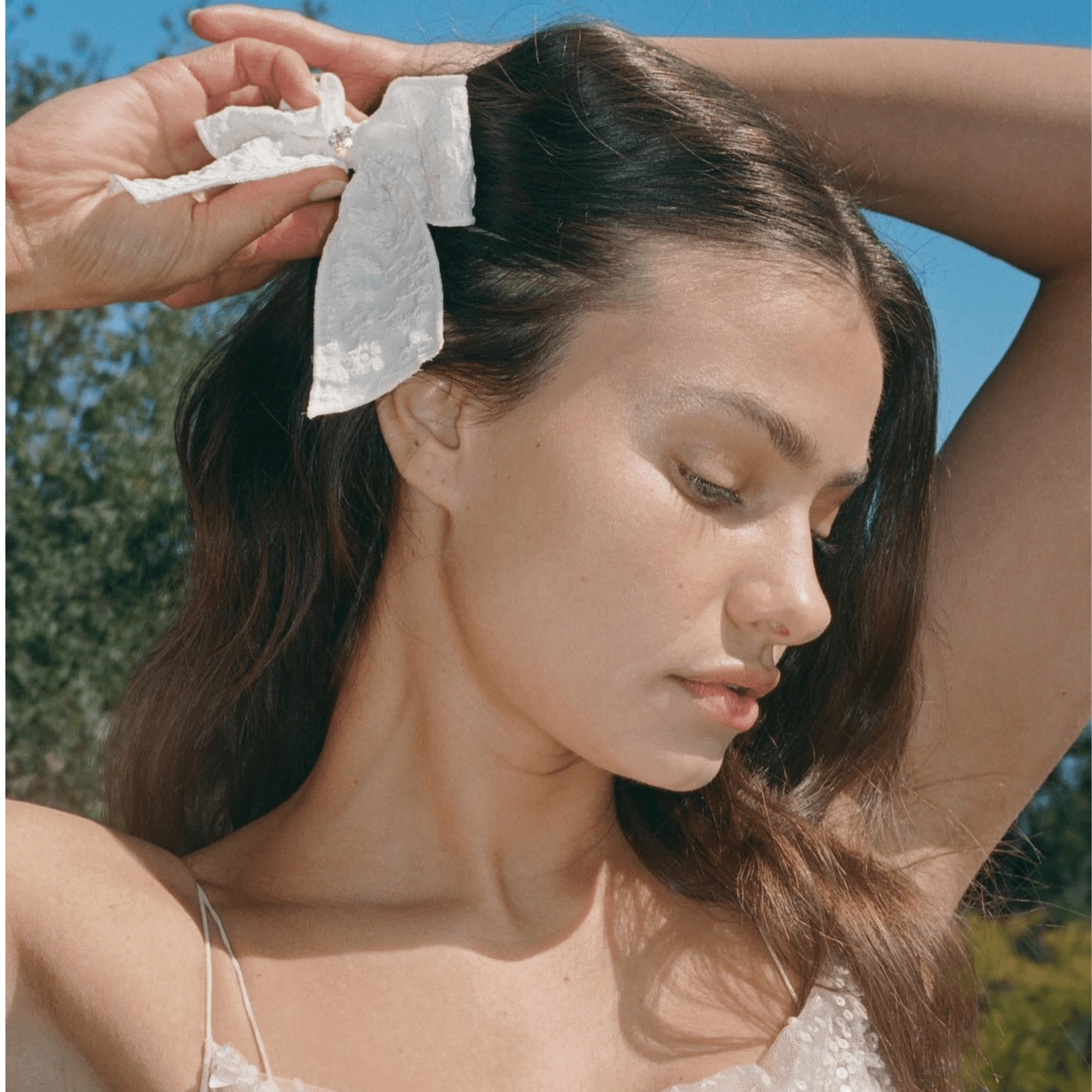 Close up of a model looking of camera, wearing a white bow that it holding back her side bangs.