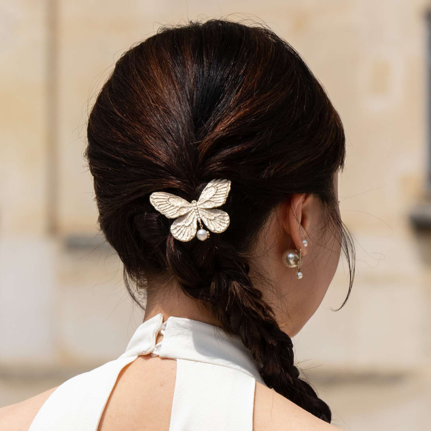 A guest at Paris Fashion Week wears a butterfly pearl hair clip at the top of her fishtail side braid