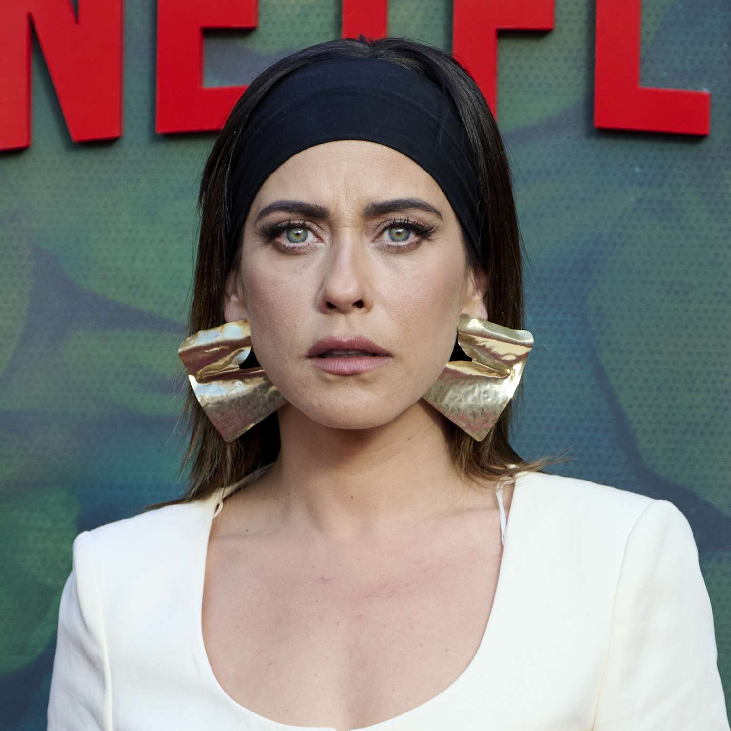 Maria Leon attends a Netflix premiere wearing a wide spandex headband and large gold structural earrings